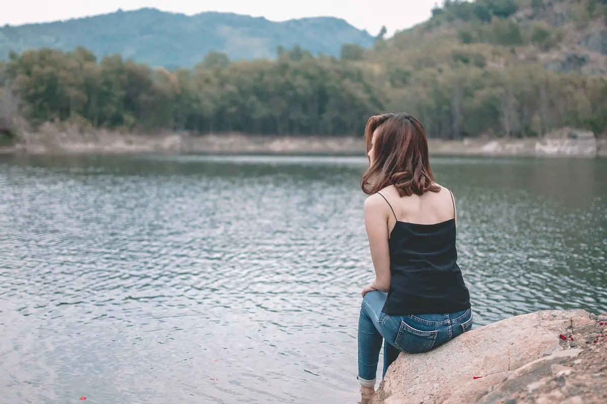 A woman sitting by a lake, lost in thought